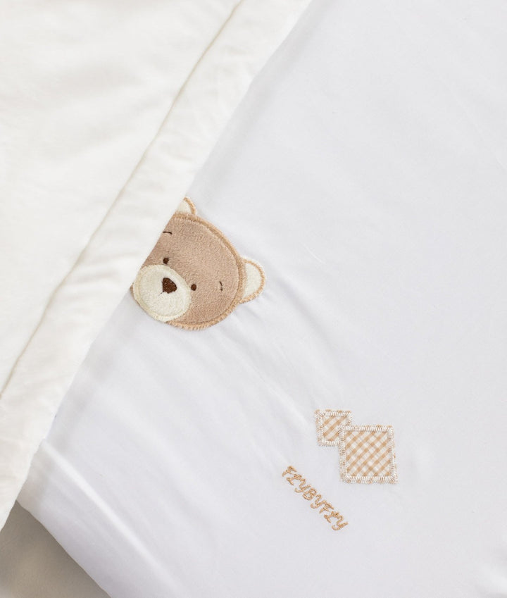 White cotton fitted sheet detail with embroidered brown bear face and gingham diamond motifs