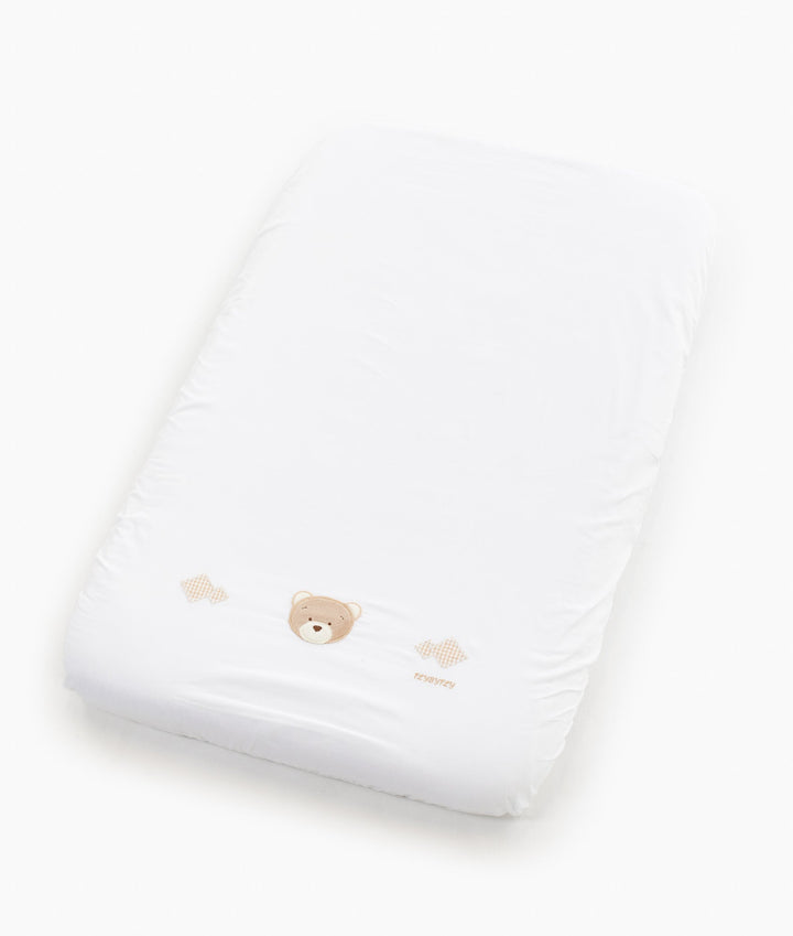 White 100% cotton fitted sheet stretched over bassinet mattress with central bear embroidery