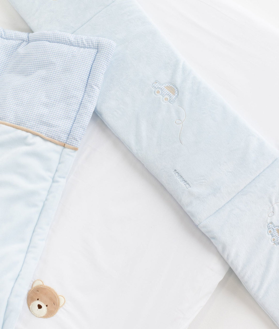 Bassinet set details: embroidered cars on bumper, tan trim, and bear patch on sheet