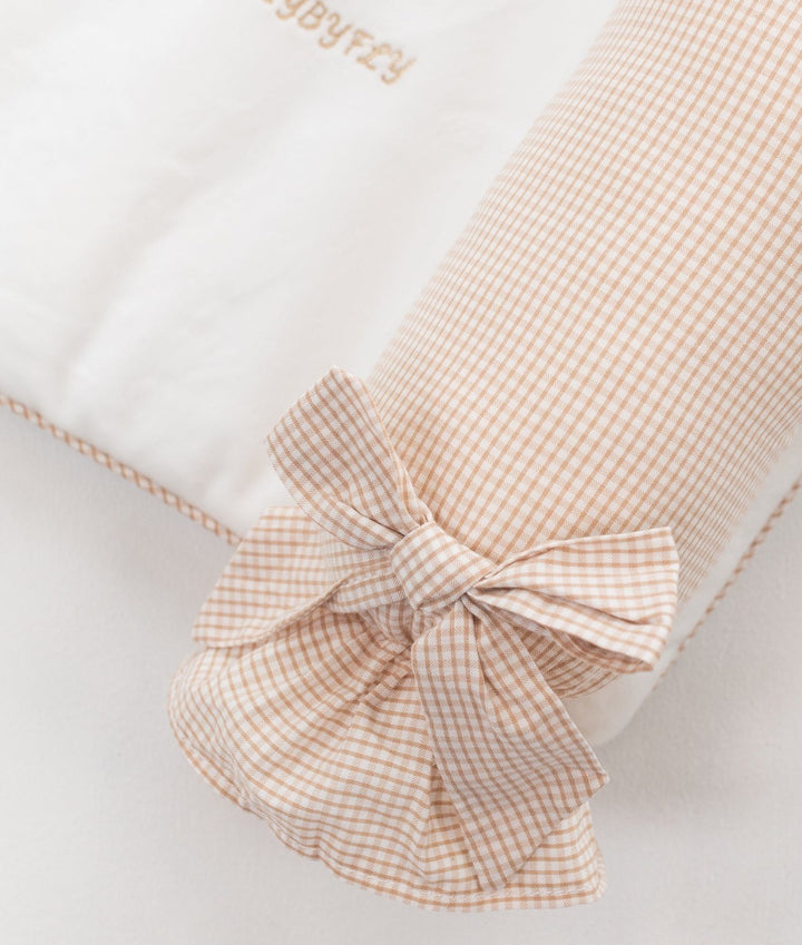 Detail of beige gingham cotton bow tied on cylindrical change mat bolster