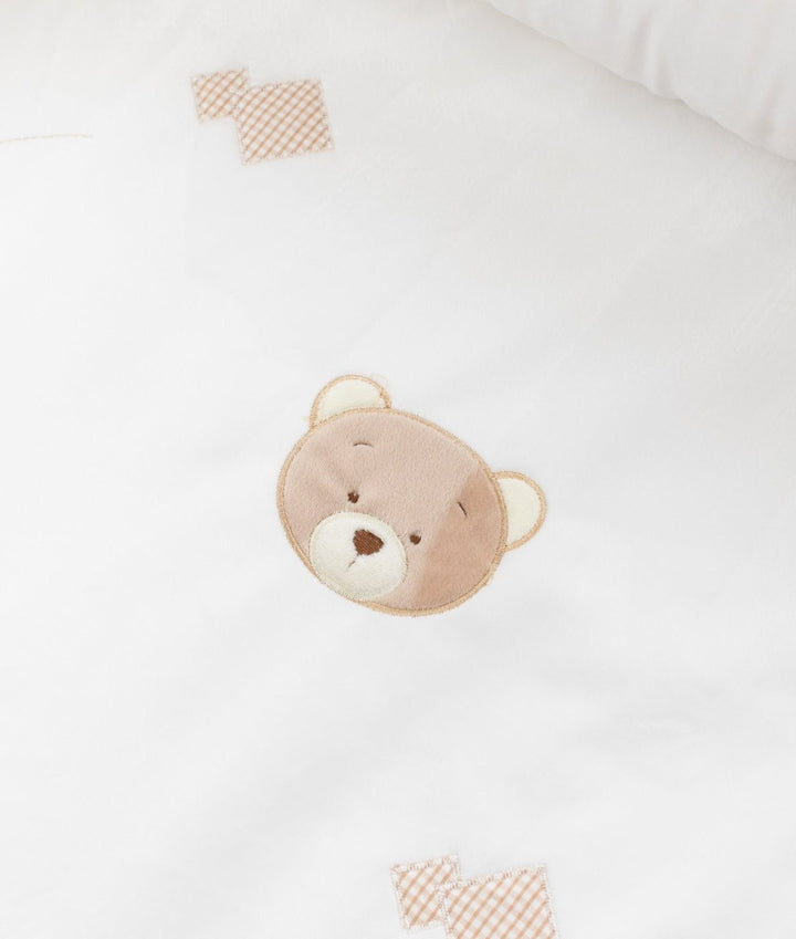 Macro detail of teddy bear applique patch on white cotton with beige gingham squares
