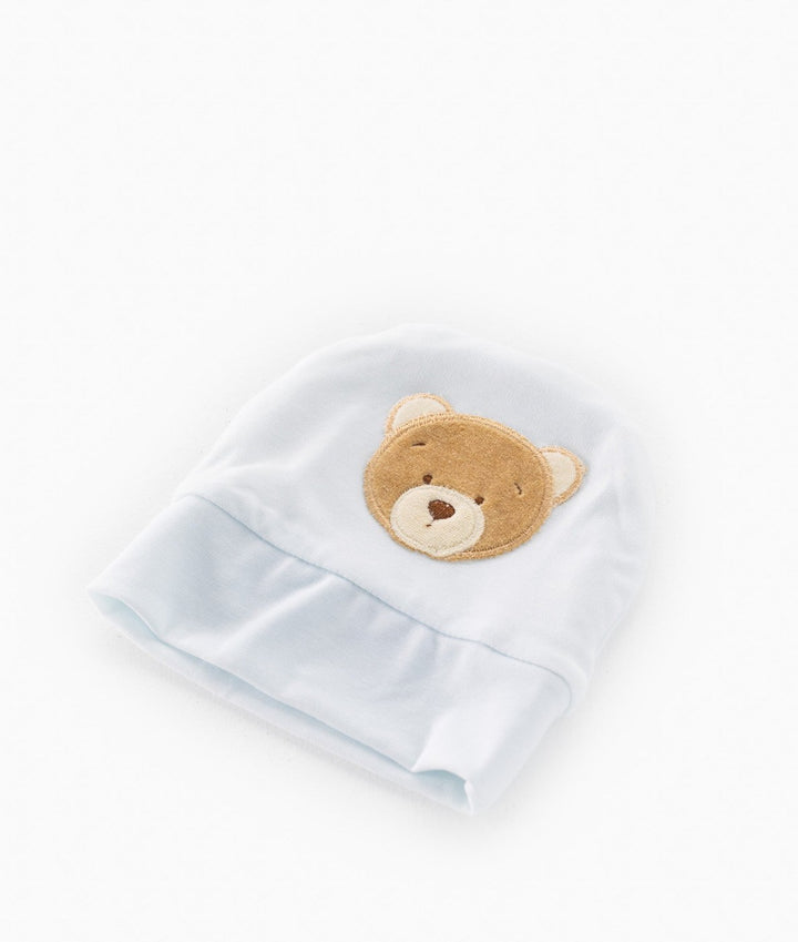angled studio shot of pale blue baby toque highlighting plush texture of bear patch and soft cotton drape