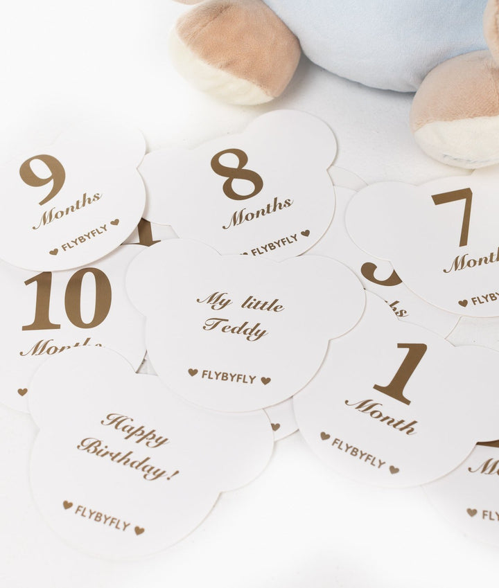 Set of white die-cut baby milestone cards with gold text and blue bear feet