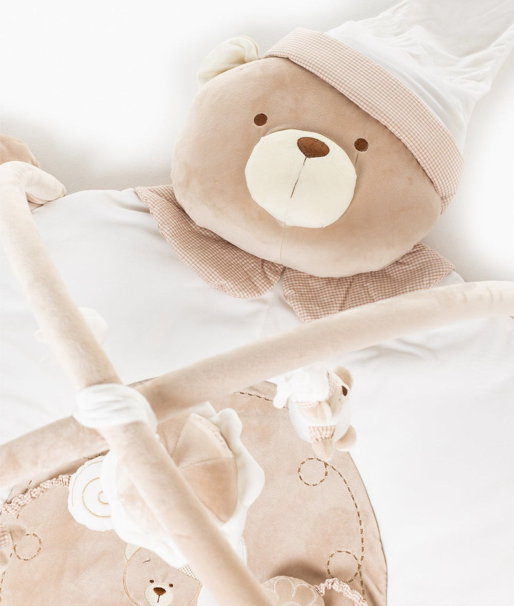 Beige plush bear head pillow with white nightcap and gingham trim on soft velvet playmat