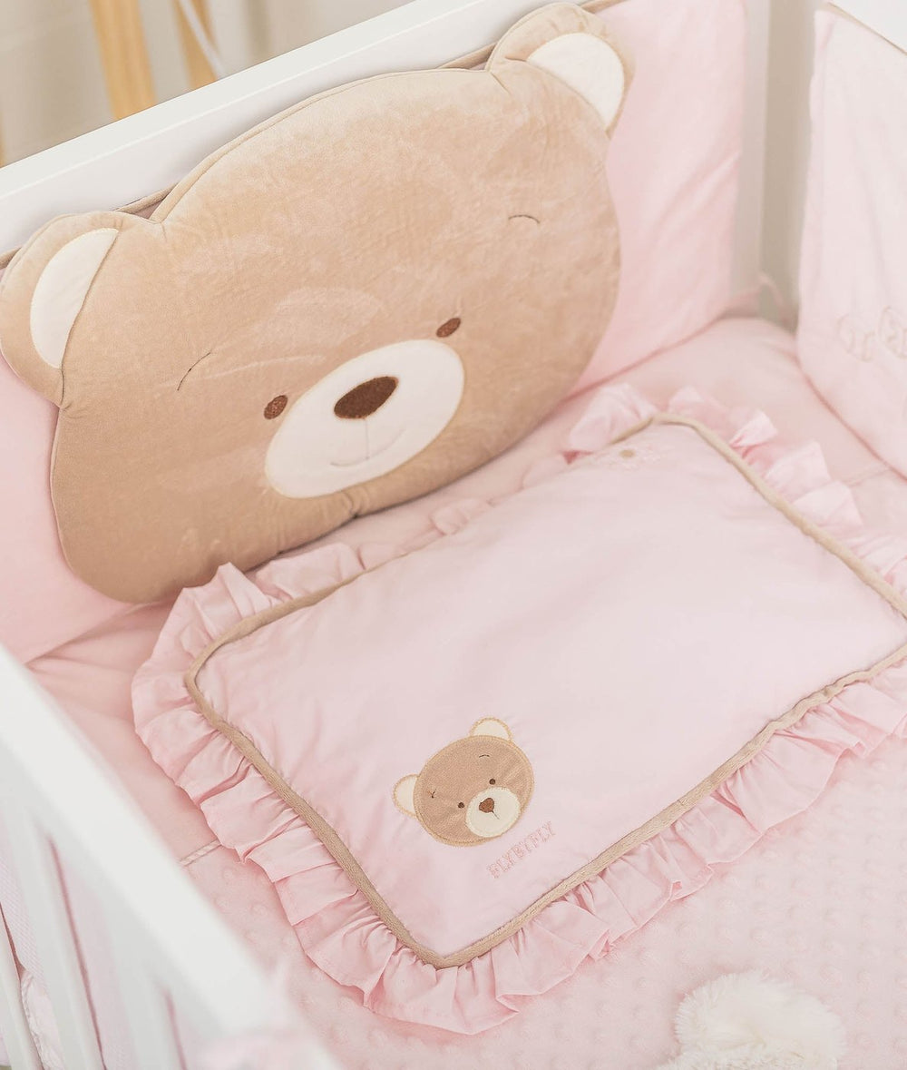 Cot arrangement with plush tan bear back cushion and ruffled pink pillow on dotted quilt