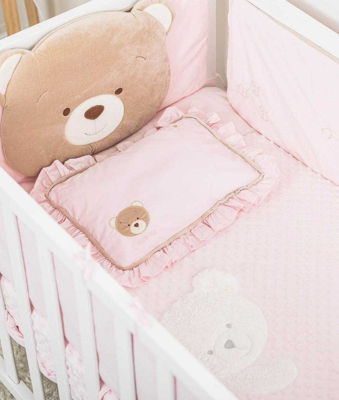 Complete pink toddler bedding set with tan bear pillow, ruffled cot pillow, and bubble dot sheet