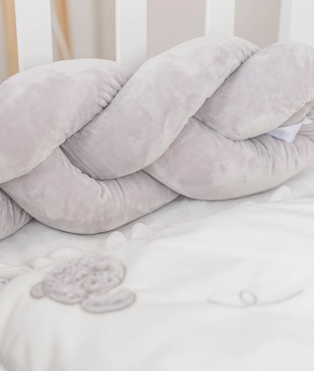 light grey braided velvet crib bumper against white slats with bear quilt