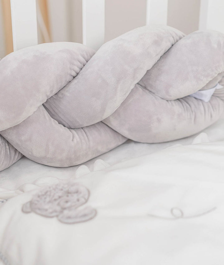 light grey braided velvet crib bumper against white slats with bear quilt