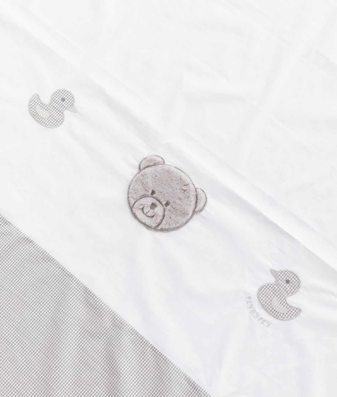 Angled view of white flat sheet with grey gingham ducks and plush bear center