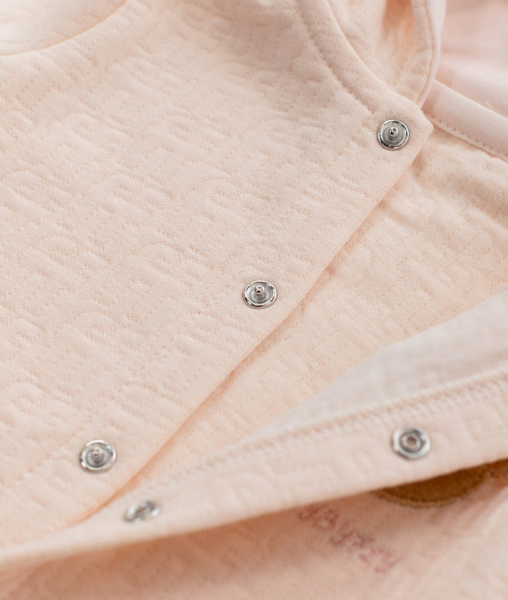 Close-up of light pink cotton fabric with embossed texture and silver snaps