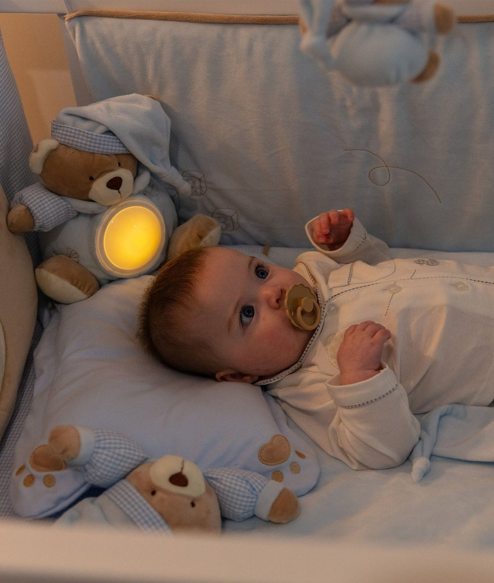 Blue teddy bear night light glowing warmly in a crib beside sleeping baby
