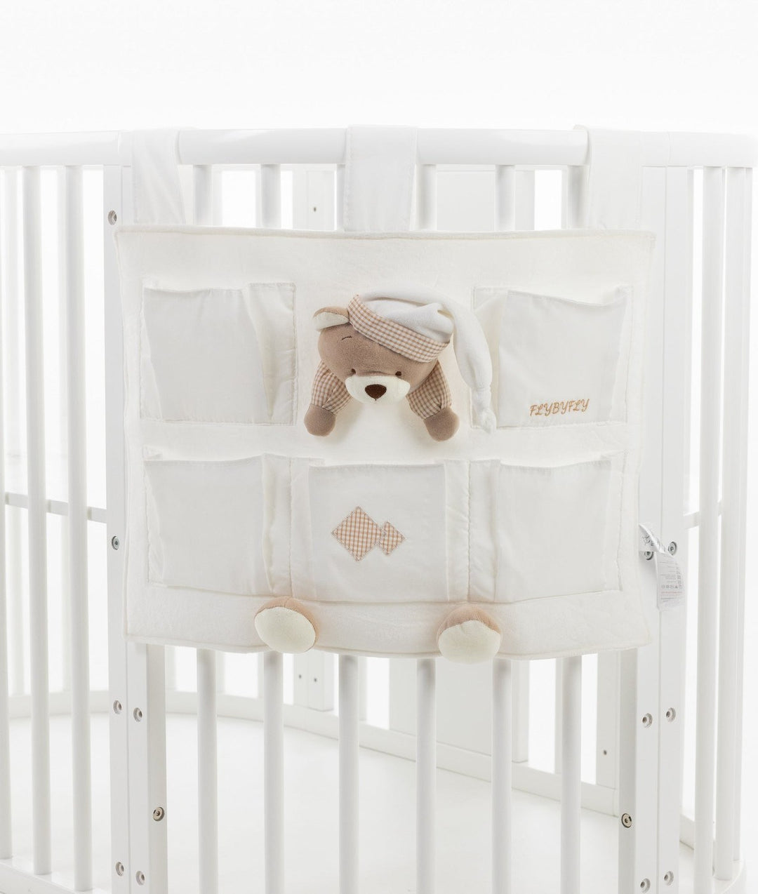 Cream colored hanging nursery storage caddy with multiple compartments and beige checkered trim mounted on white baby crib