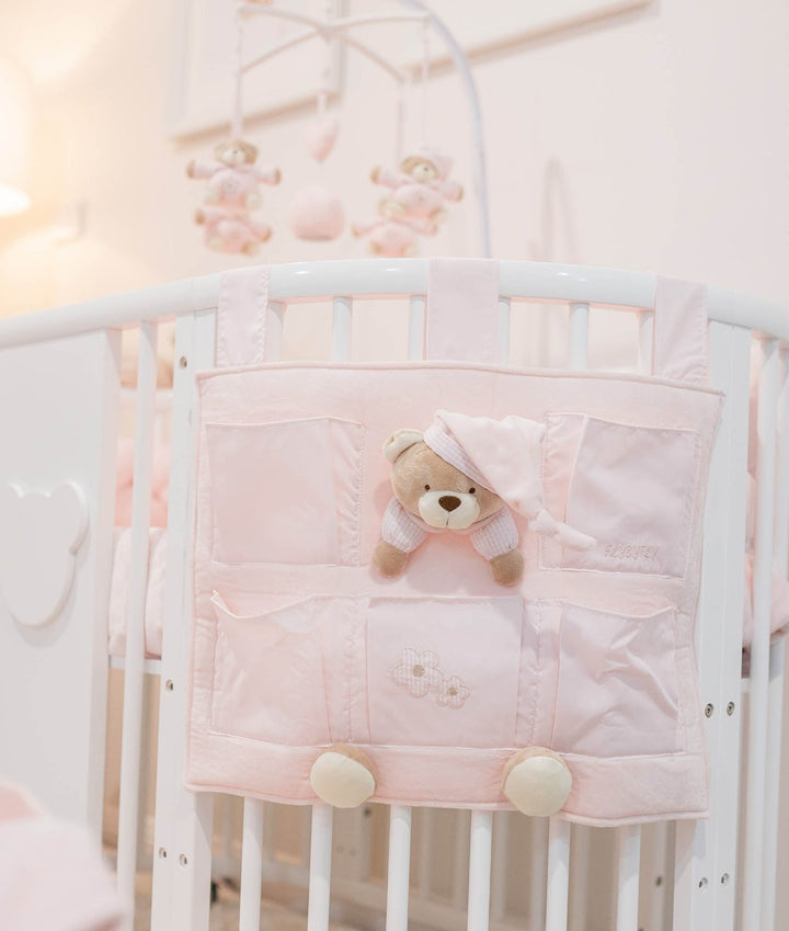 Pink fabric crib organizer bag with multiple pockets and stuffed bear attachment