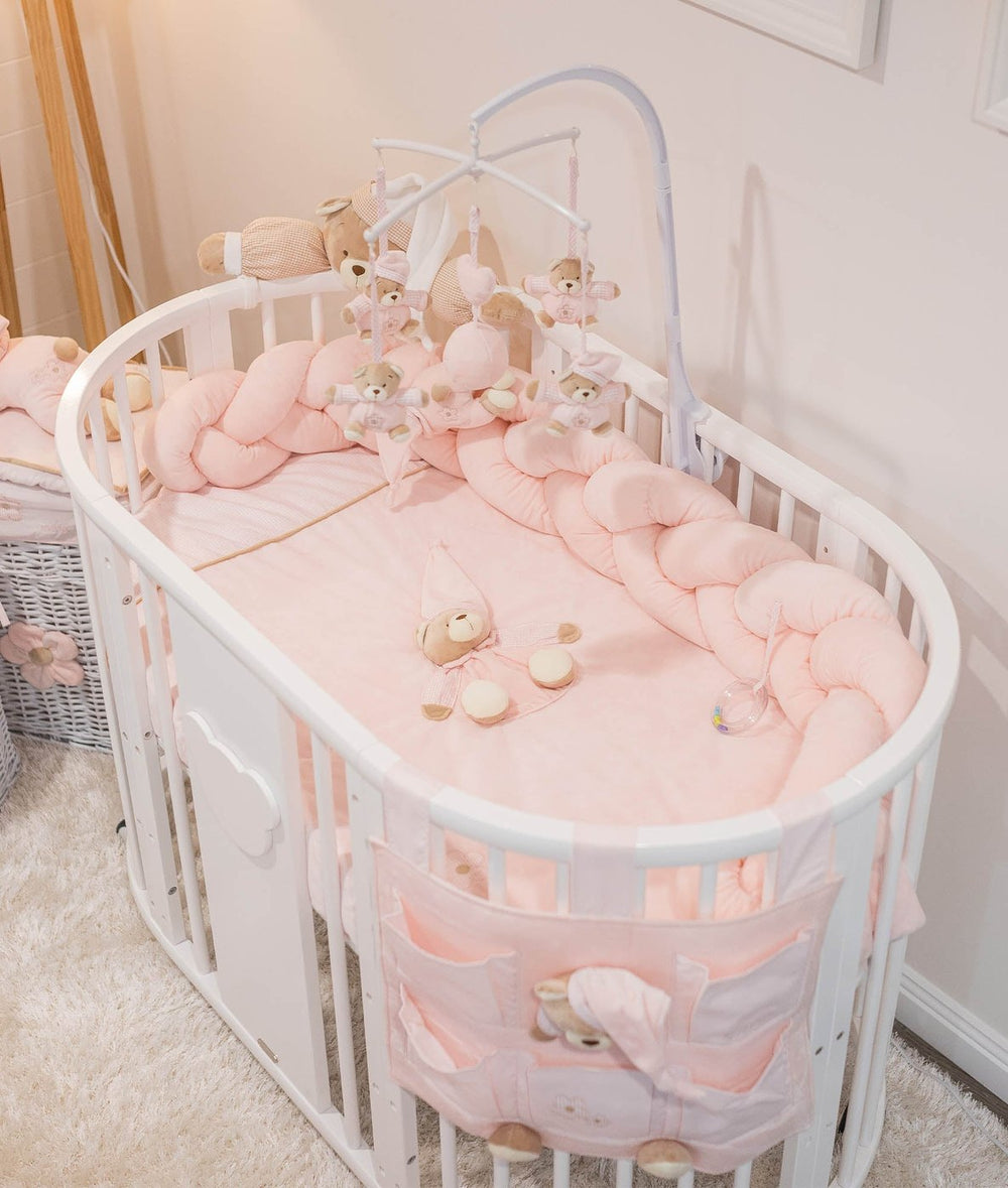 Signature Bear Cot with pastel pink braided bumper, fitted sheet, and storage organizer