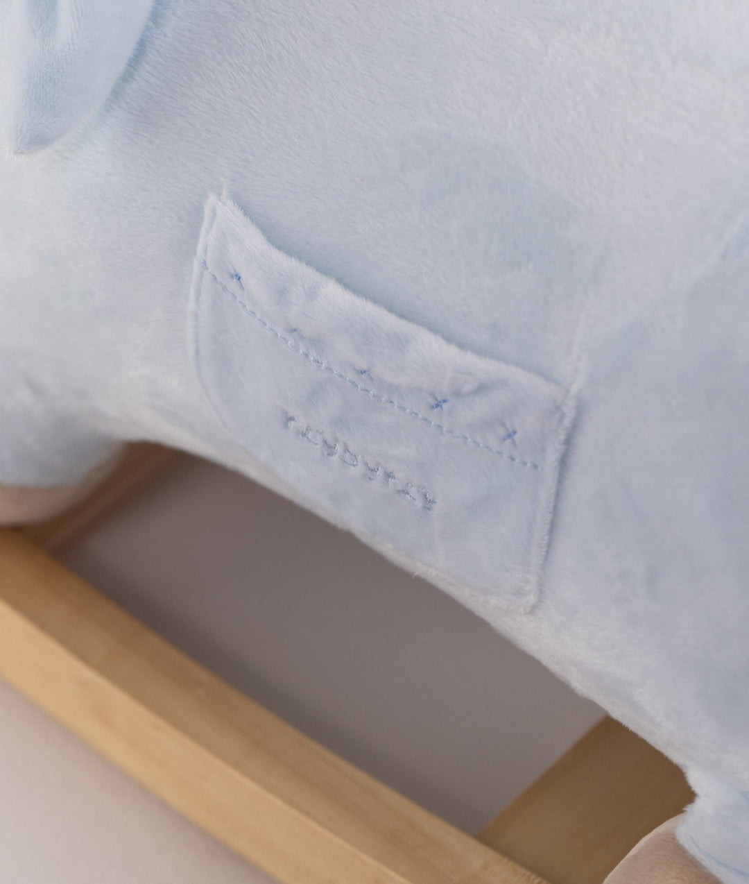 Close-up of light blue plush texture and stitched patch above natural wood base