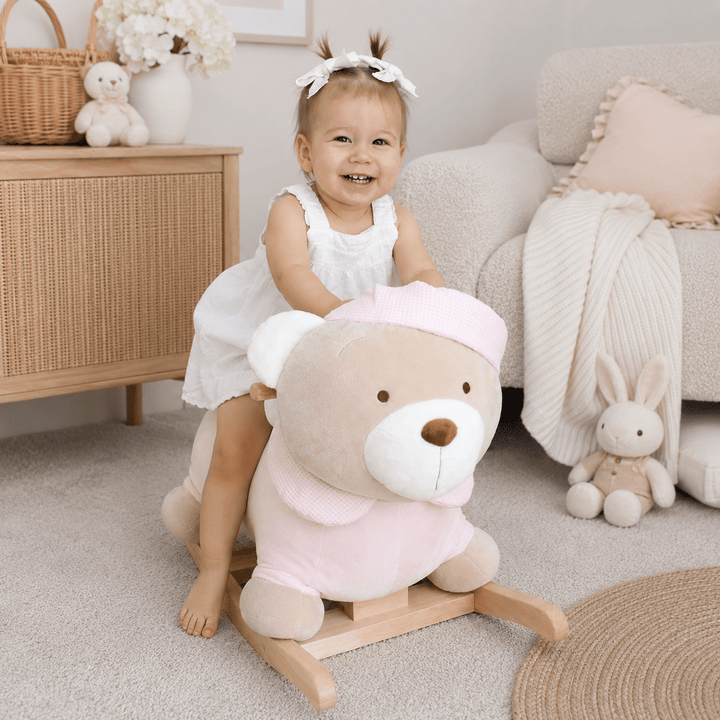 Toddler sitting on pink rocking teddy bear in nursery