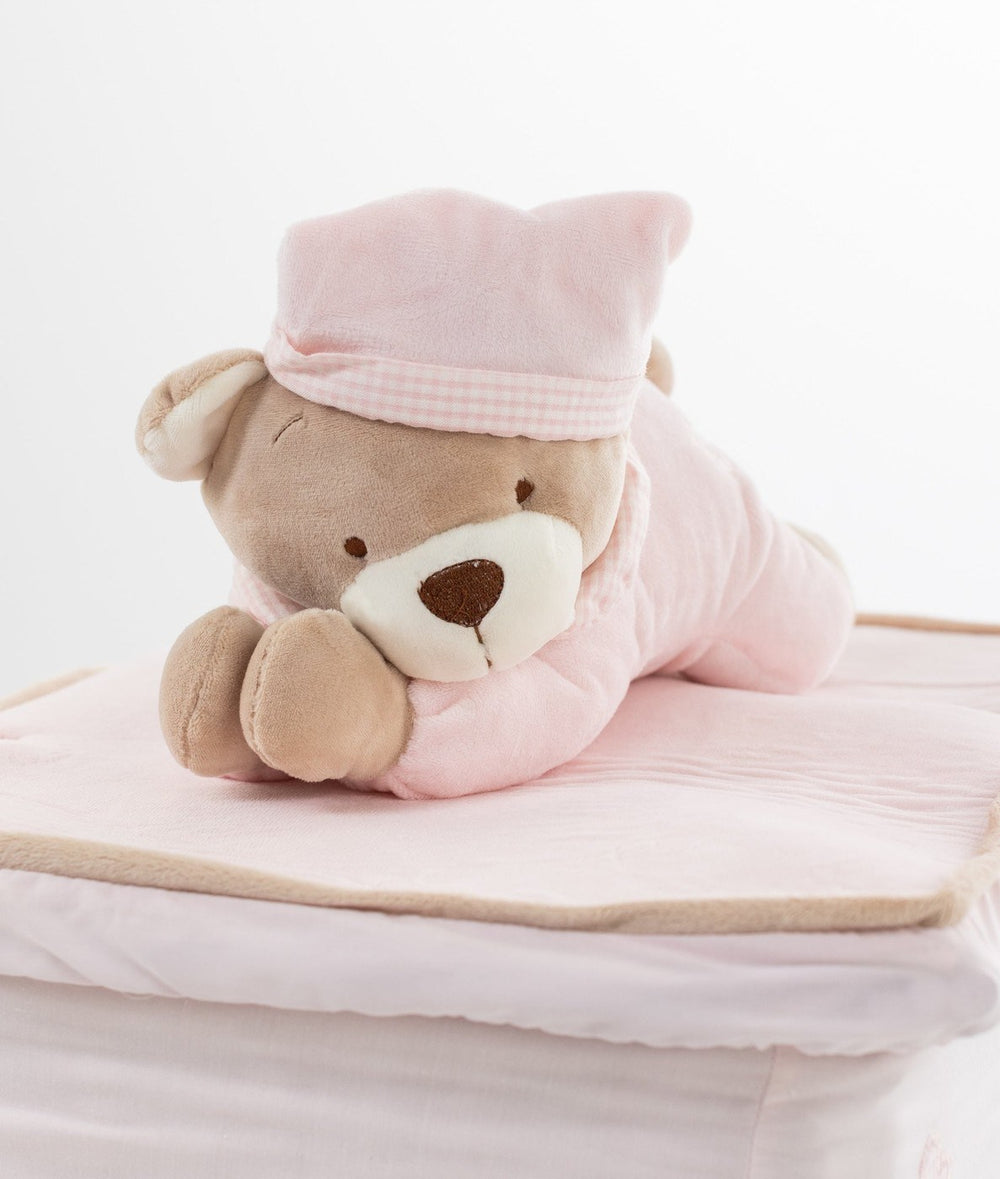 Teddy bear in pink quilted onesie lying on soft padded wicker basket lid