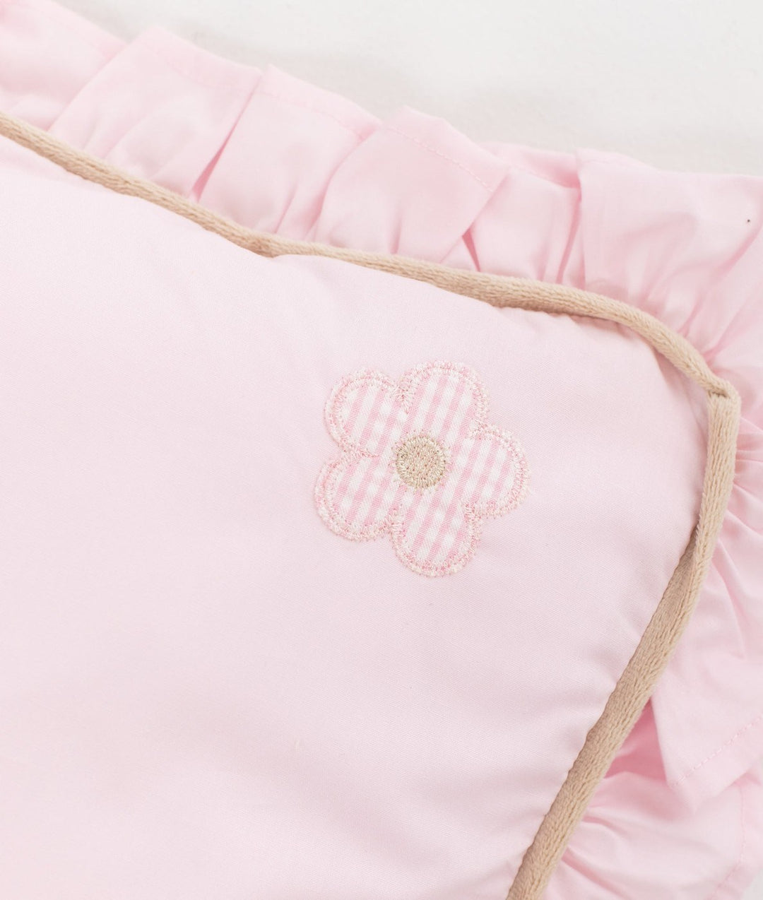 Close up of pink cotton pillow corner with gingham flower patch and beige piping