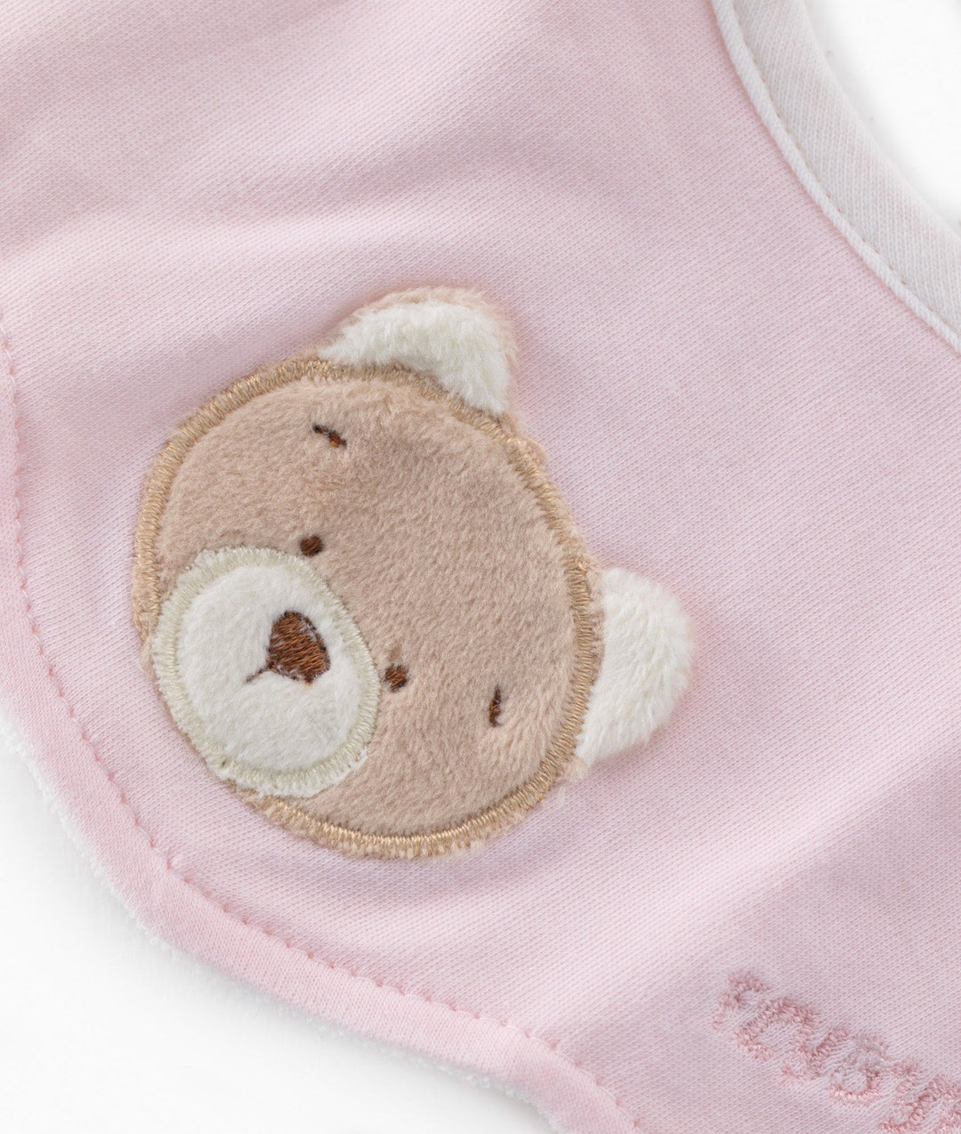 Close-up of pink baby bib teddy bear patch with embroidered face and scalloped edge